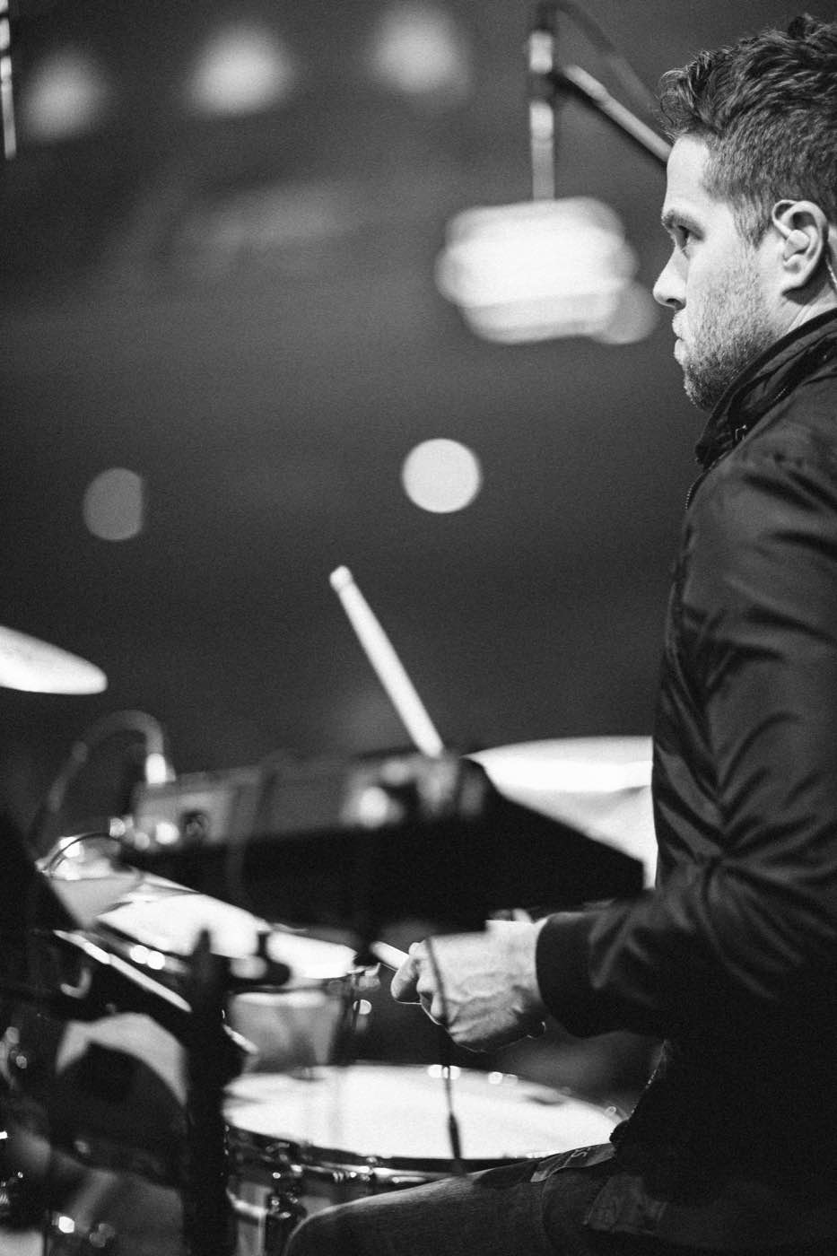 Black and white close-up of a drummer playing, side profile, dramatic lighting.
