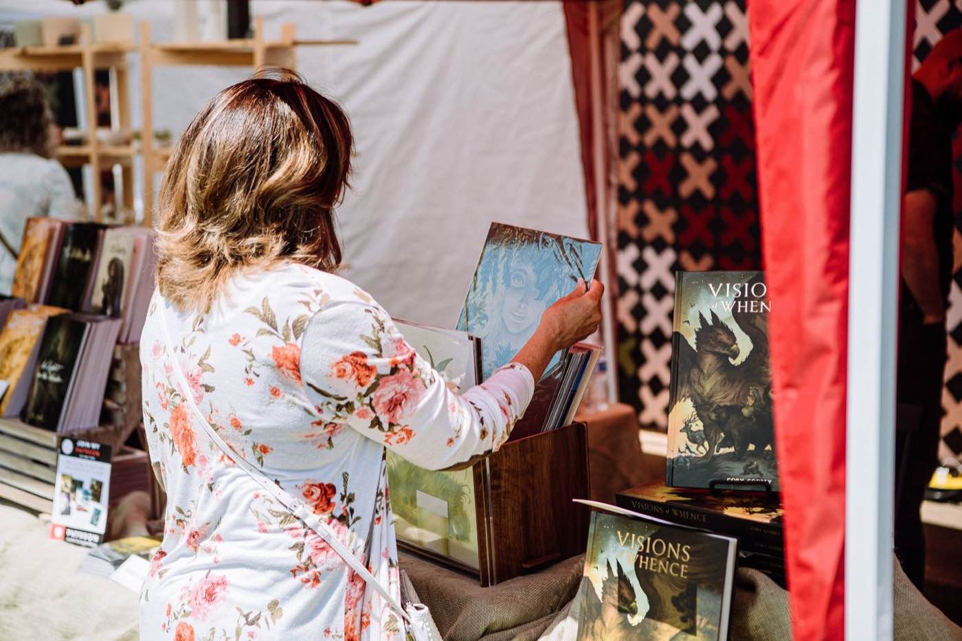 Woman in floral shirt browsing books at an outdoor market, soft natural light