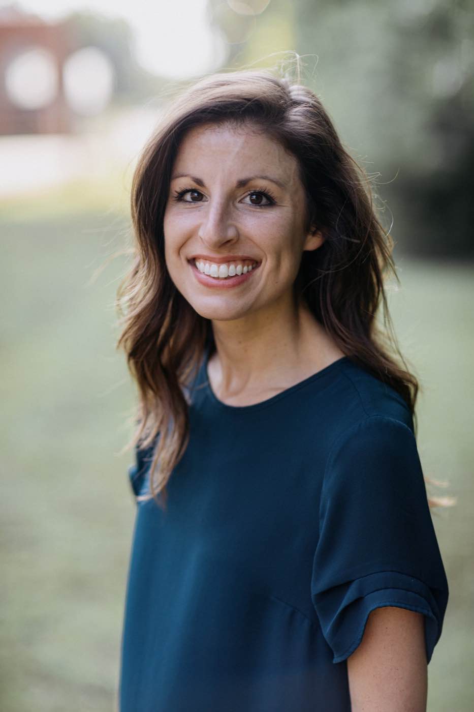 Close-up outdoor portrait of a smiling woman with warm, natural lighting and a soft background.