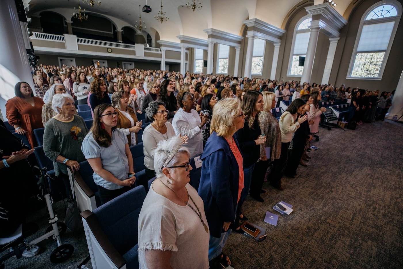 Wide shot of a large group of women standing in a church, looking forward with soft, natural light.