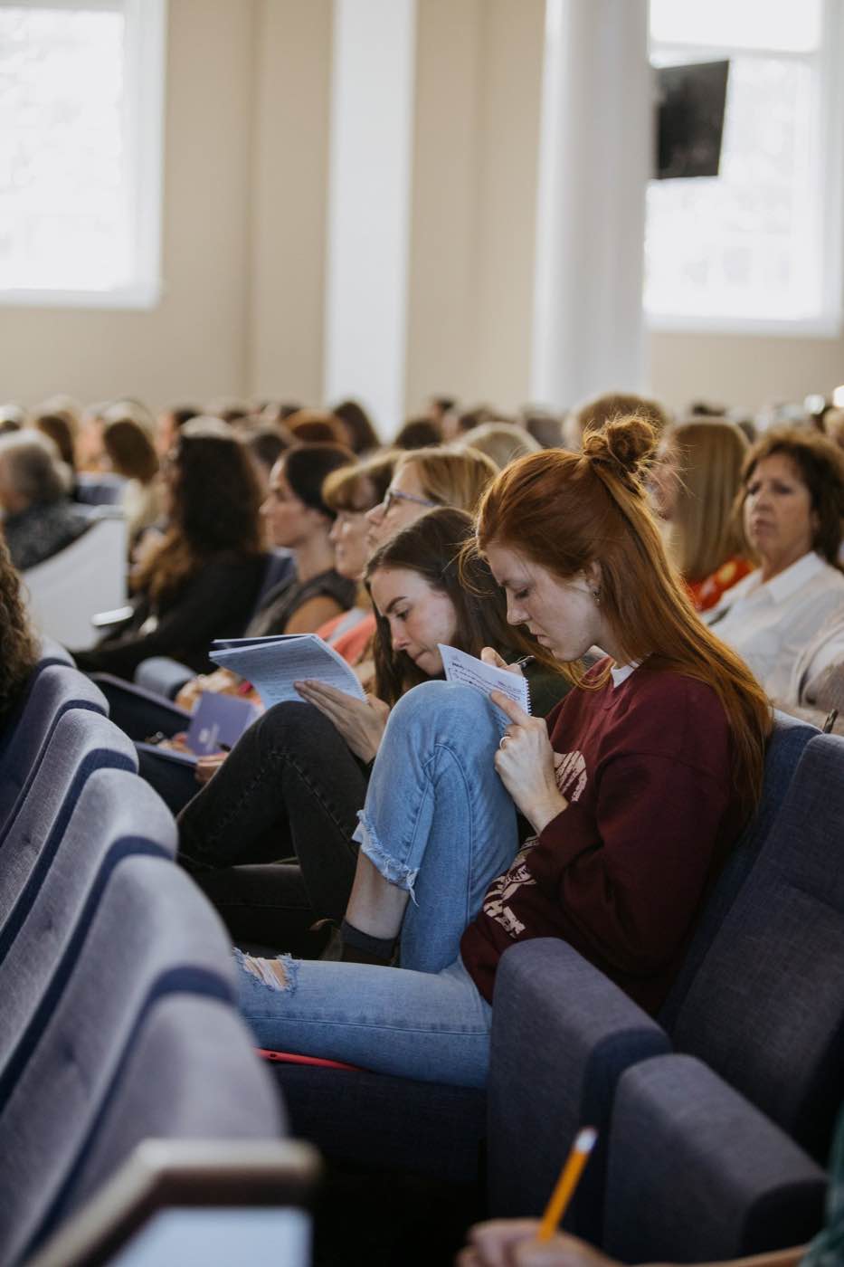 Attendees at a conference or lecture, focused on notes in a well-lit room, creating an attentive mood.
