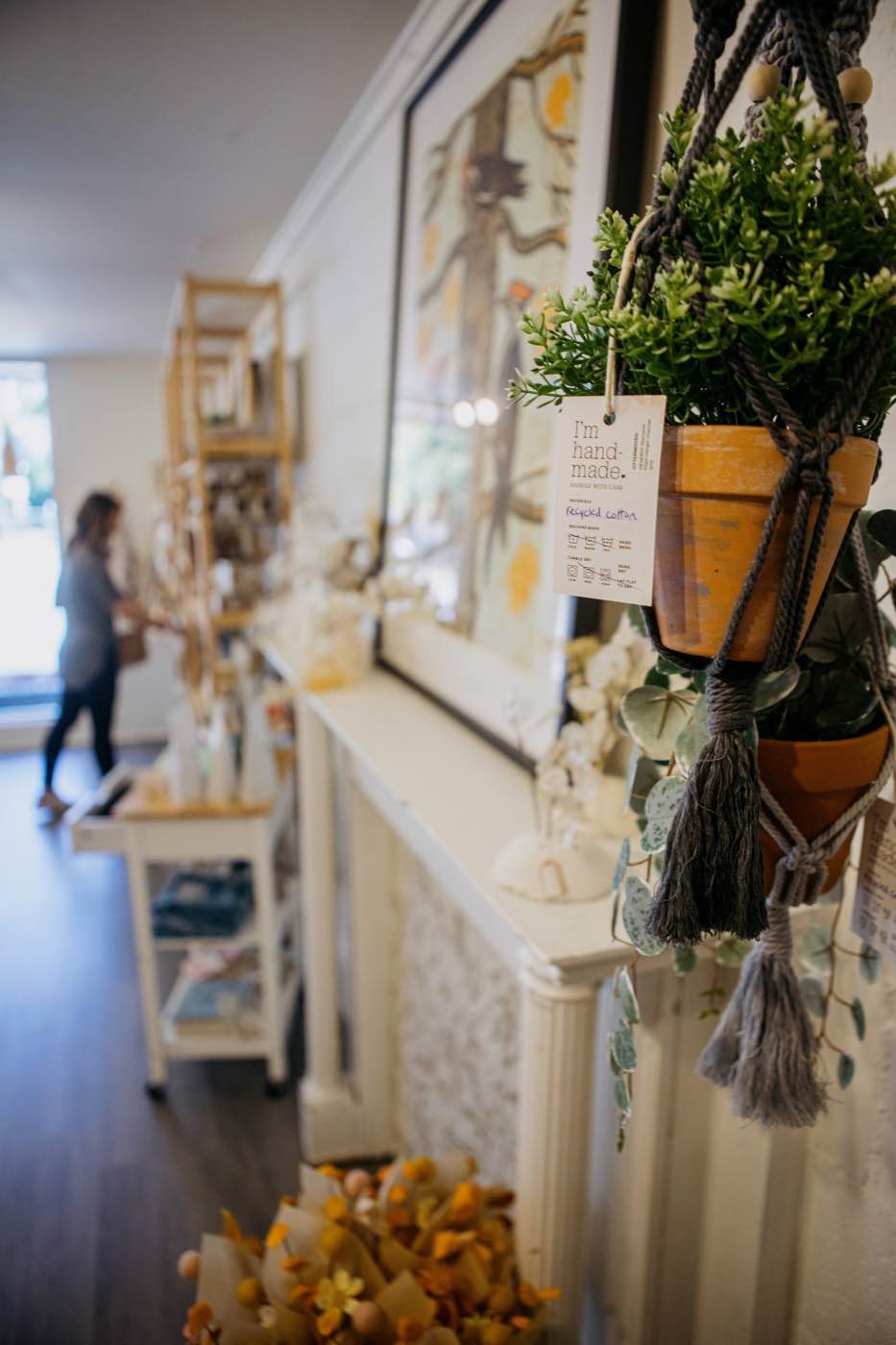 Close-up of a handmade macrame plant hanger with a terracotta pot, in a bright store.