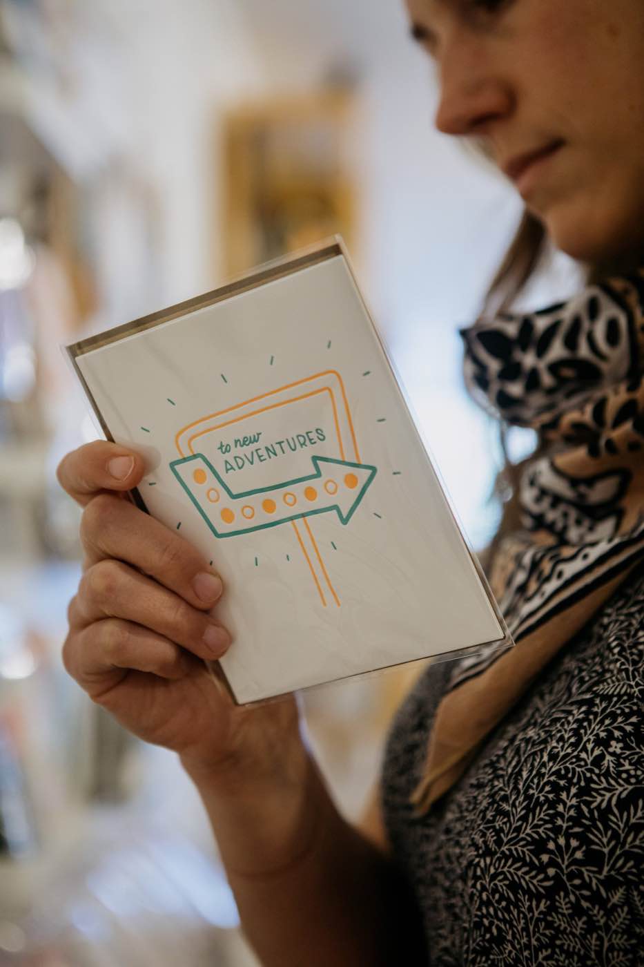 Close-up of a person holding a greeting card with 'to new adventures' text, soft natural light.