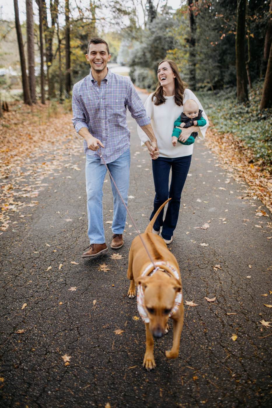 Joyful family of three and their dog walking on an autumn path, natural light, warm mood.