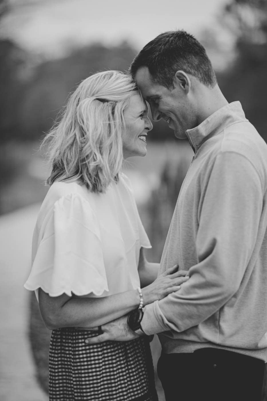 Black and white portrait of a couple, foreheads touching, smiling intimately in soft light.