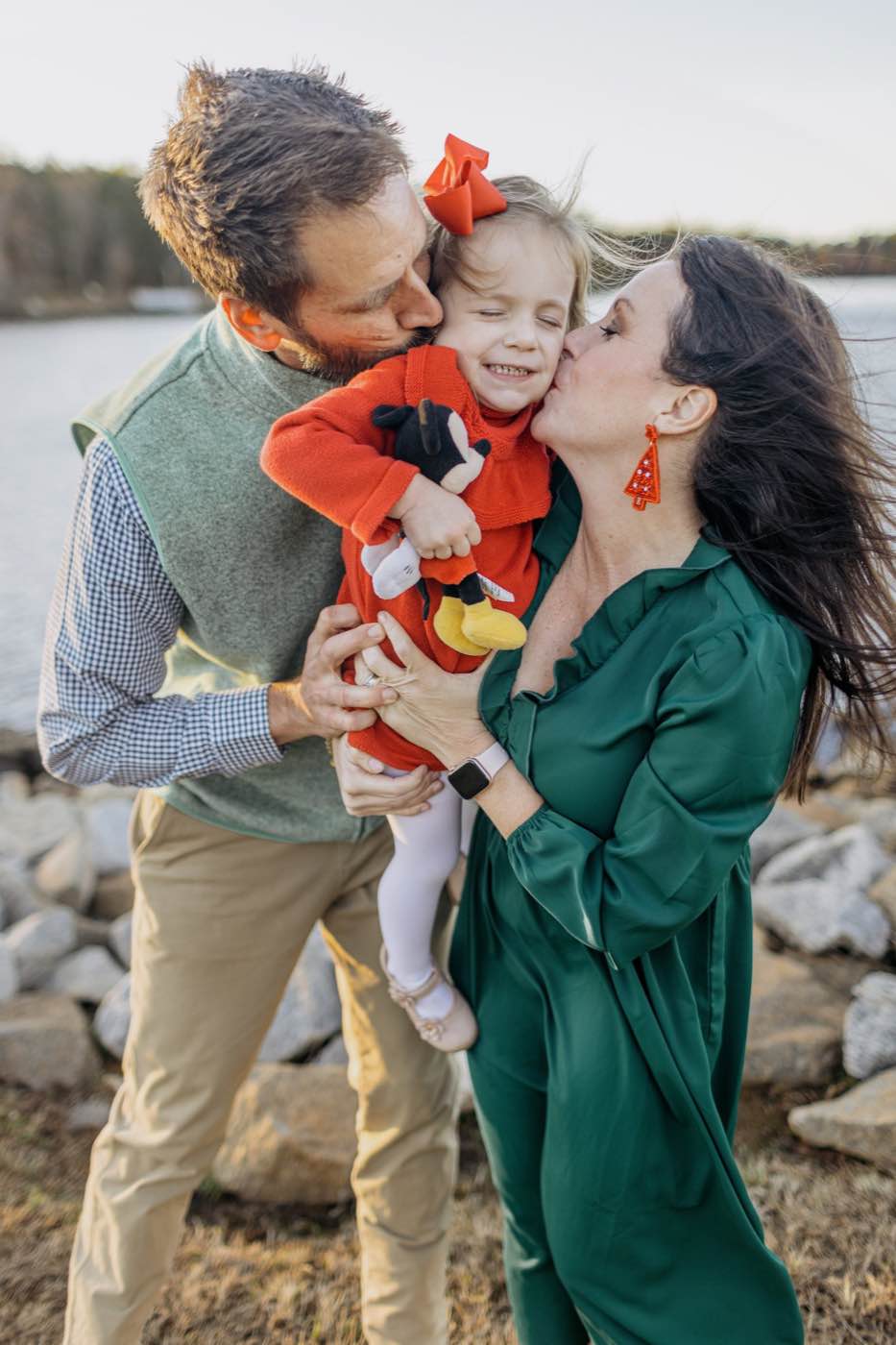Warm, intimate portrait of a family of three by a lake at sunset, soft golden hour light.
