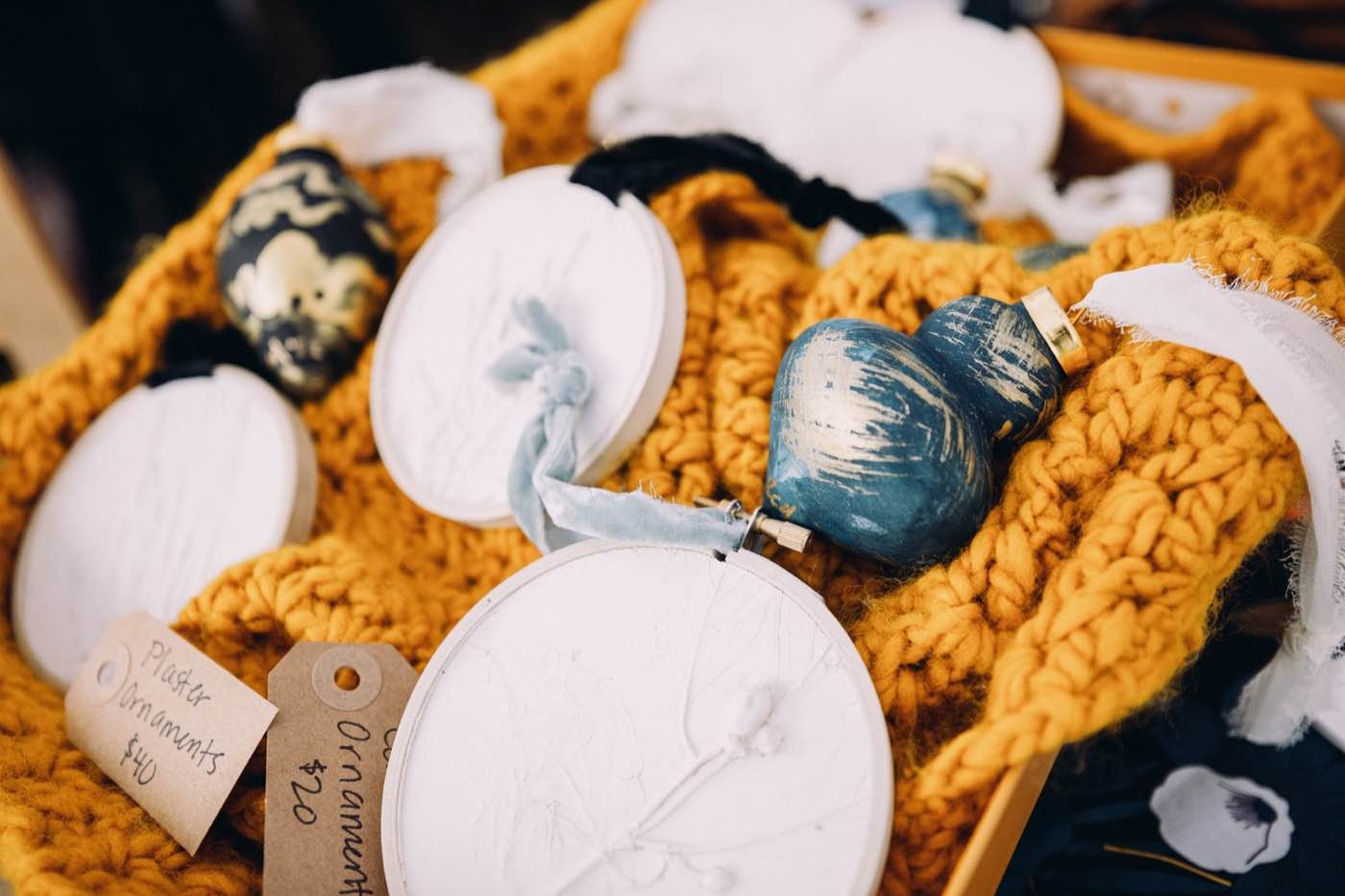 Close-up of handmade plaster ornaments and a blue heart-shaped ornament on a mustard yellow knitted blanket.