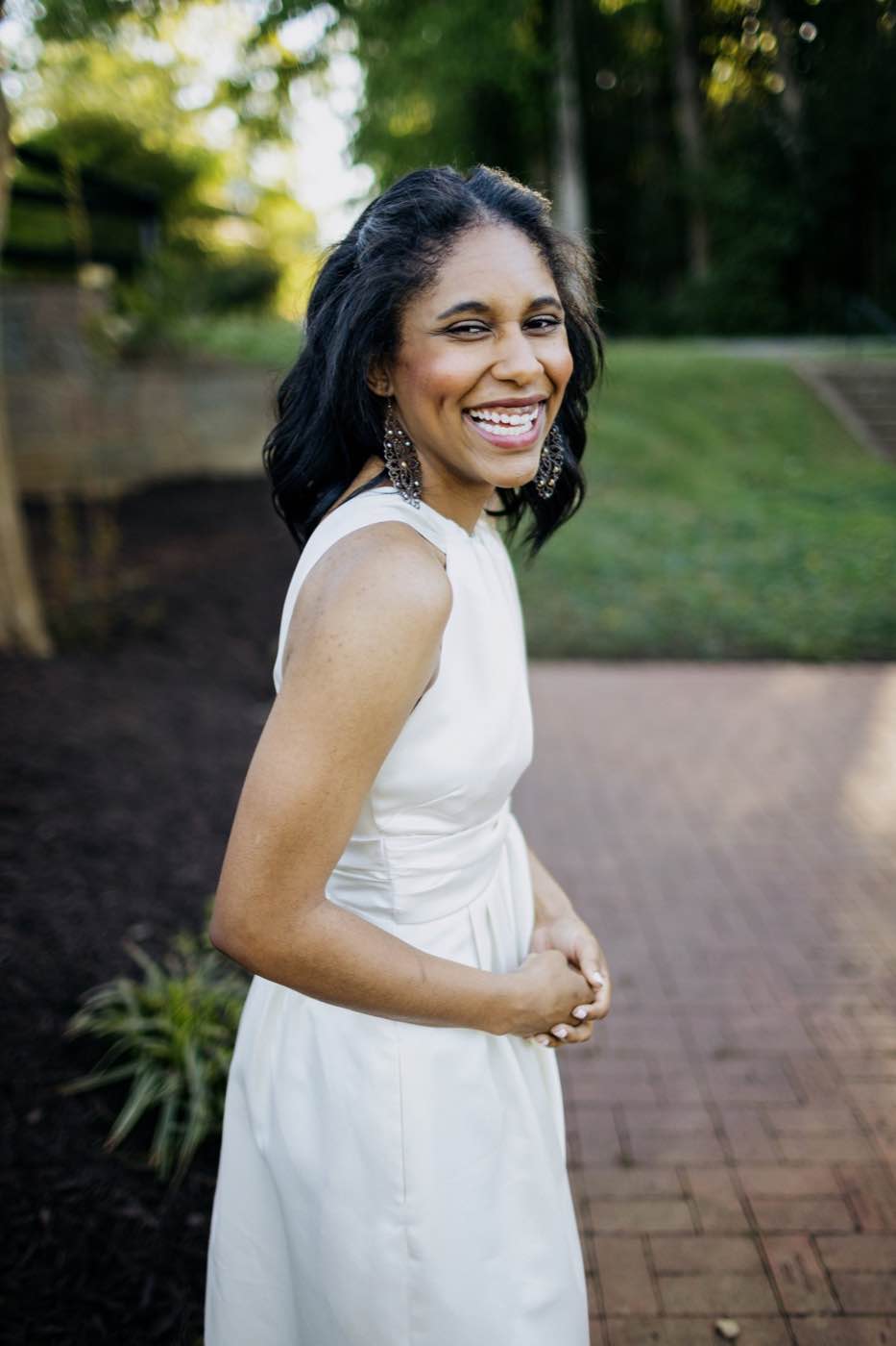 Joyful woman in white dress, laughing outdoors with soft natural light and green background.
