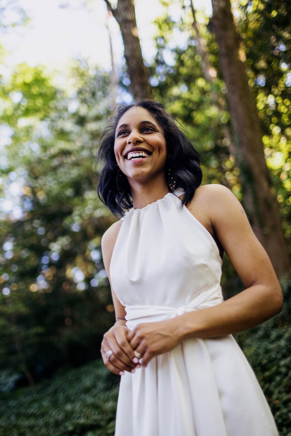 Joyful woman in a white dress smiling outdoors with natural light and bokeh background.