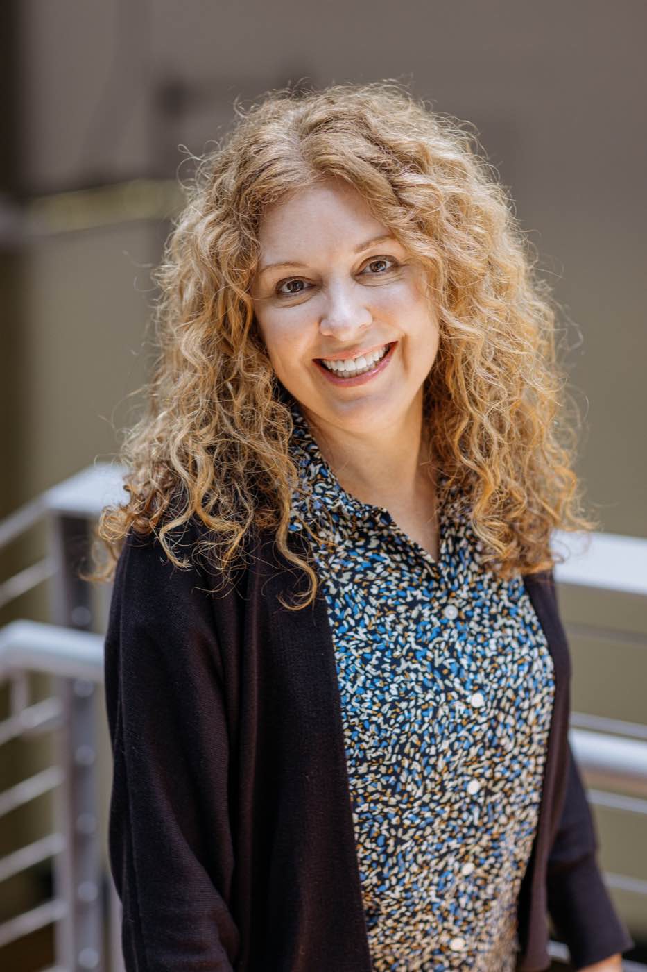 Smiling woman with curly hair in a well-lit indoor setting, natural light, joyful mood.