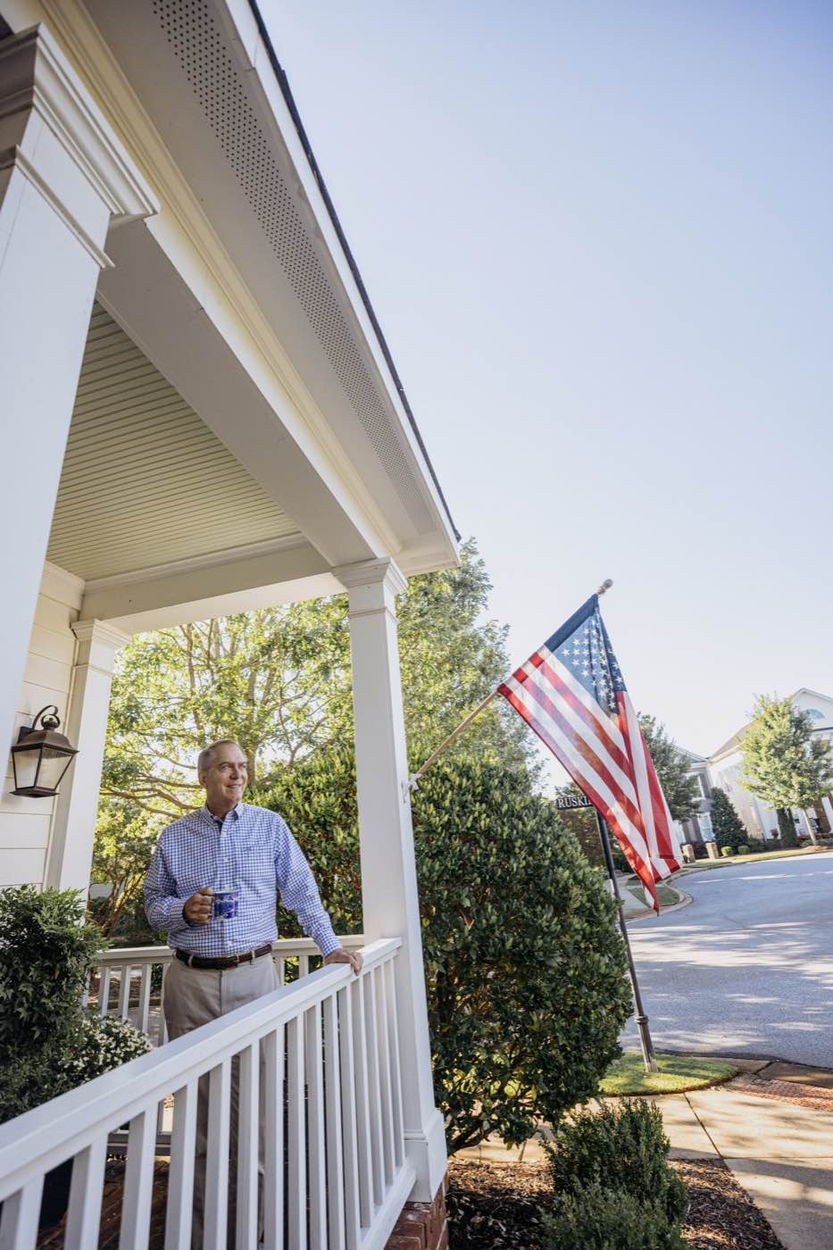 Man on a porch with an American flag, bathed in warm morning light, serene mood.