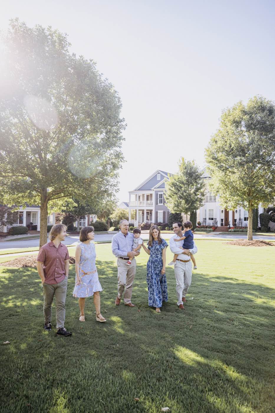 Group walking across a sun-drenched lawn during a portrait session in a suburban neighborhood.