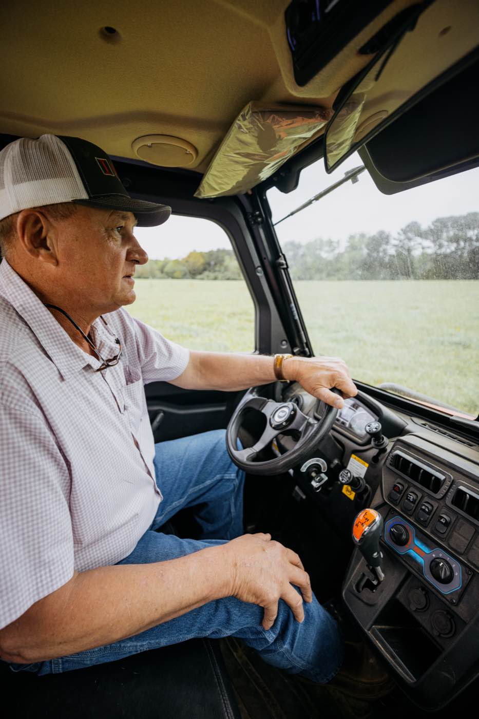 Man in a utility vehicle, looking out at a green field under an overcast sky.