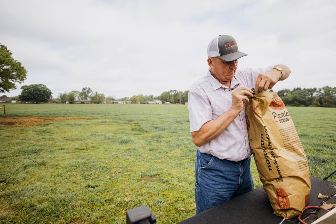 Man in a field opening a feed bag under an overcast sky, natural light.
