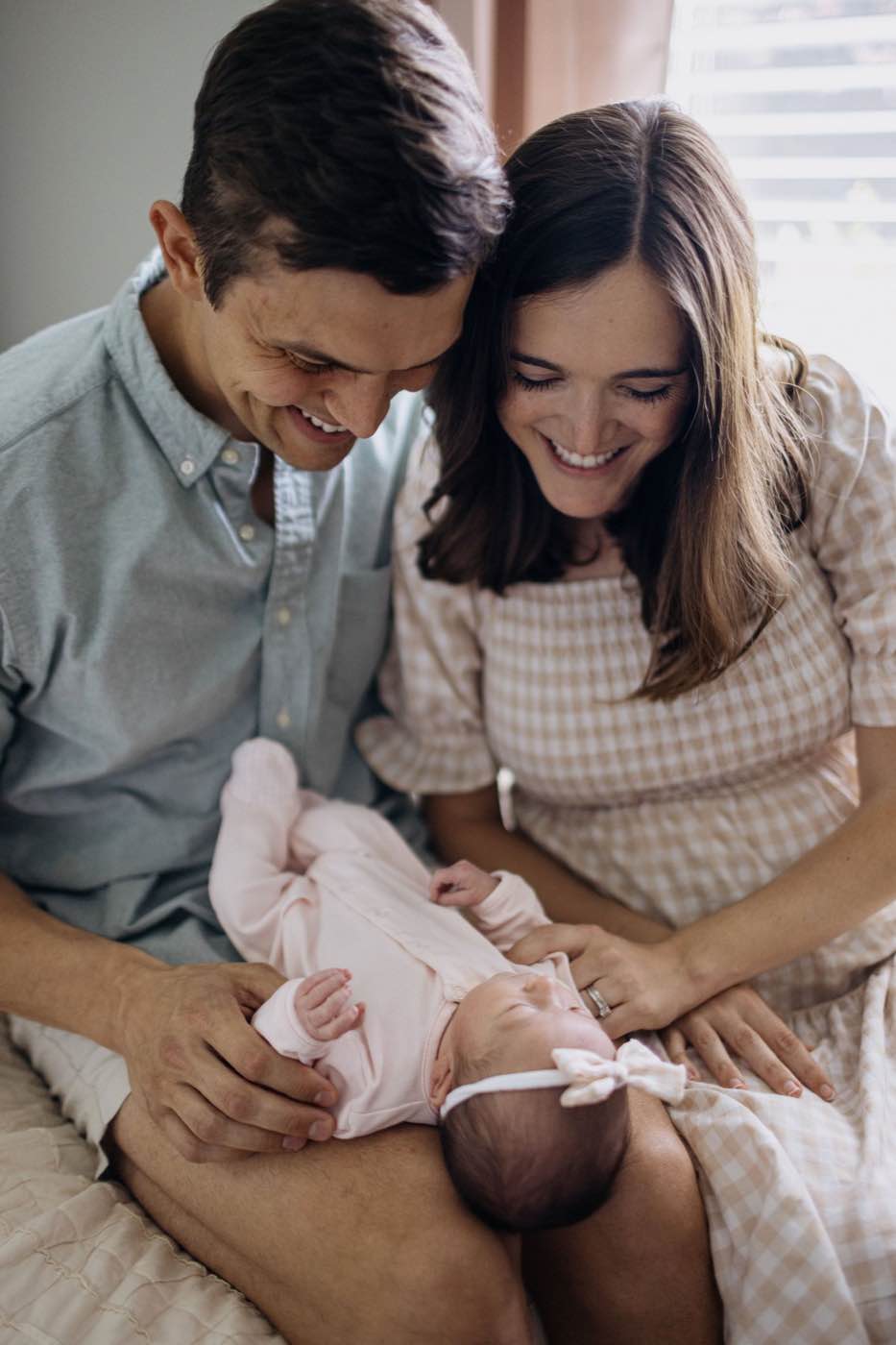Softly lit portrait of a joyful couple looking down at their newborn baby, creating an intimate mood.
