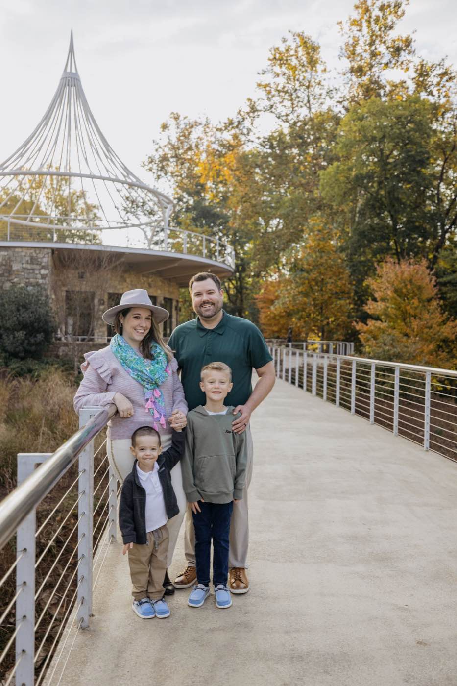 Joyful family of four on a bridge with autumn trees and a unique gazebo in soft, natural light.