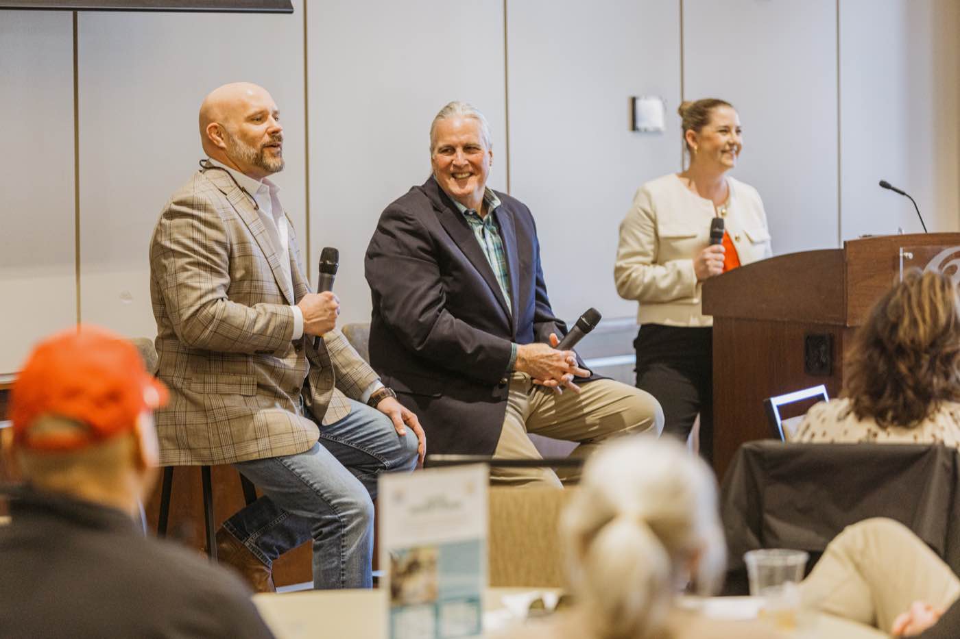 Three panelists, two men and one woman, speaking at a corporate event with warm lighting.